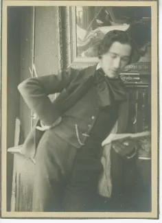 portrait photographique d’André Gide, accoudé à un buffet, lisant, une main sur la hanche