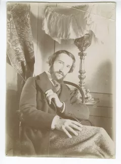 portrait photographique d’André Gide assis, à la barbe en double pointe, une main sur le col de sa veste, dans sa chambre du Royal-Hôtel, février-mars 1895