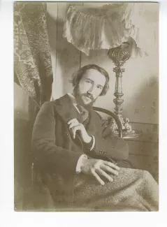 portrait photographique d’André Gide assis, à la barbe en double pointe, une main sur le col de sa veste, dans sa chambre du Royal-Hôtel, février-mars 1895