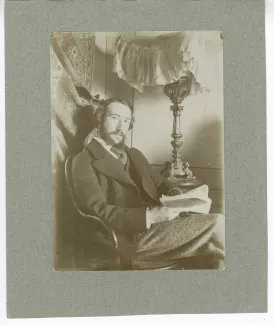 portrait photographique d’André Gide assis, à la barbe en double pointe, un livre entre les mains, dans sa chambre du Royal-Hôtel, février-mars 1895