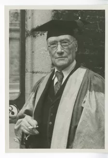 portrait photographique en buste d’André Gide, en costume de docteur Honoris Causa de l'Université d'Oxford, devant un portail, 7 juin 1947