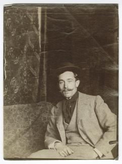 portrait photographique de Paul-Albert Laurens, assis devant un tapis suspendu au mur