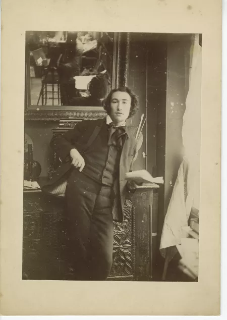 portrait photographique d’André Gide, accoudé à un buffet, tenant un livre, la main droite dans sa poche de veston
