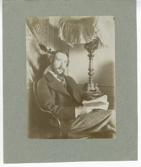 portrait photographique d’André Gide assis, à la barbe en double pointe, un livre entre les mains, dans sa chambre du Royal-Hôtel, février-mars 1895