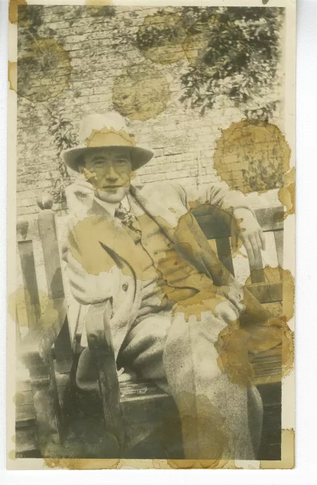 photographie d’André Gide, avec chapeau, assis sur un banc, fumant, à Garsington Manor, Oxfordshire, chez Lady Ottoline Morrell, lors de son séjour en Angleterre avec Marc Allégret, août 1920