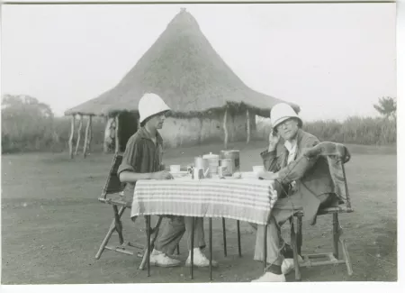 photographie de Marc Allégret et André Gide, avec son petit primate Dindiki sur le dossier de sa chaise, tous deux portant un casque colonial, attablés devant un gîte d'étape