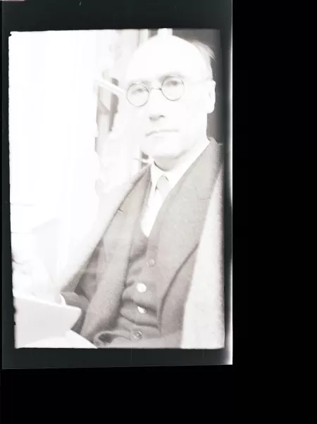 portrait photographique en buste d'André Gide, regardant l'objectif, avec lunettes, main droite près d'un livre, juillet 1931