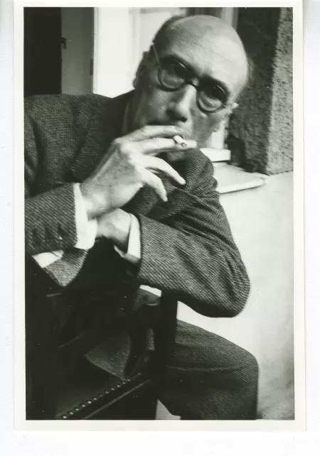 portrait photographique d'André Gide, de face, avec lunettes, cigarette à la bouche, à califourchon sur une chaise, juillet 1931