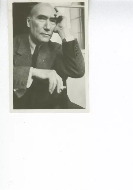portrait photographique en buste d'André Gide, regardant l'objectif, cigarette dans la main droite, la main gauche sur le front, à califourchon sur une chaise, juillet 1931