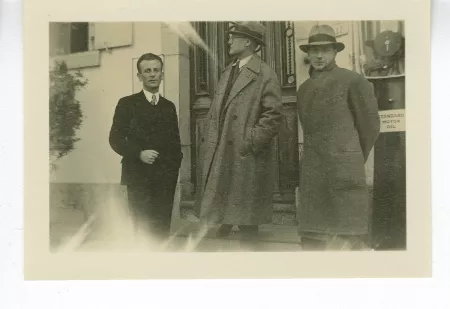 photographie d’André Gide, avec lunettes et chapeau, mains dans les poches, et les deux Bellettriens Daniel Simond, à gauche, et Pierre Beausire, à droite, devant un bâtiment, décembre 1933