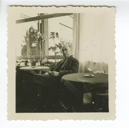 portrait photographique d’André Gide, attablé, tenant ses lunettes dans la main gauche, dans un restaurant, décembre 1933