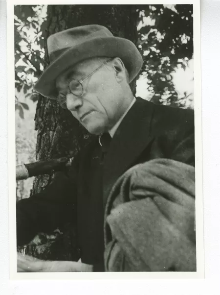 portrait photographique en buste d'André Gide, avec lunettes, chapeau et veste au bras, lisant, août 1934