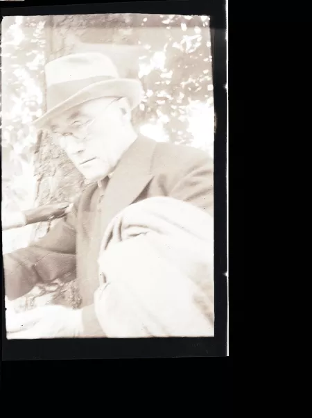 portrait photographique en buste d'André Gide, avec lunettes, chapeau et veste au bras, lisant, août 1934