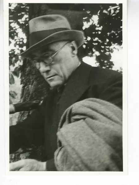 portrait photographique en buste d'André Gide, avec lunettes, chapeau et veste au bras, lisant, août 1934