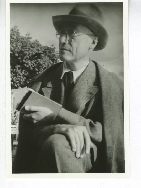 portrait photographique d'André Gide, de ¾ à gauche, avec lunettes et chapeau, la main droite sur un genou, la gauche tenant un livre, au bord du lac de Thoune, août 1934
