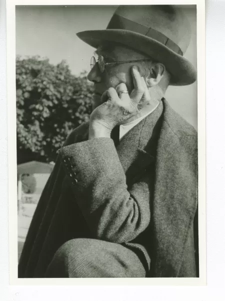 portrait photographique d'André Gide, avec lunettes et chapeau, de profil à gauche, la main gauche sur la joue et le coude gauche sur un genou, au bord du lac de Thoune, août 1934