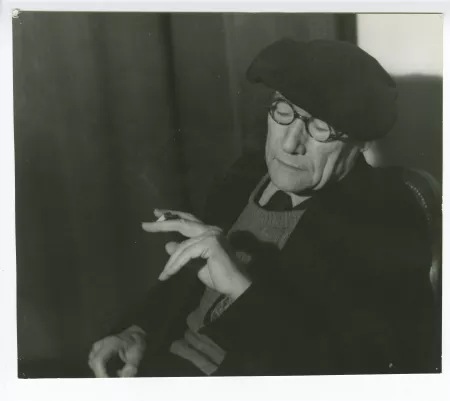 portrait photographique en buste d’André Gide, avec lunettes et béret, regardant sa cigarette, mars 1944