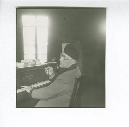 portrait photographique d’André Gide, avec lunettes et bonnet, de dos, au piano, fumant, au Vaneau