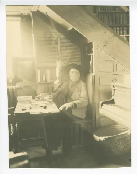 portrait photographique d’André Gide, avec lunettes et bonnet, assis à son bureau, fumant, le regard dans le vague, au Vaneau
