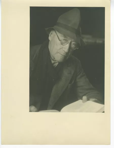 portrait photographique en buste d’André Gide, avec lunettes et chapeau, lisant un livre