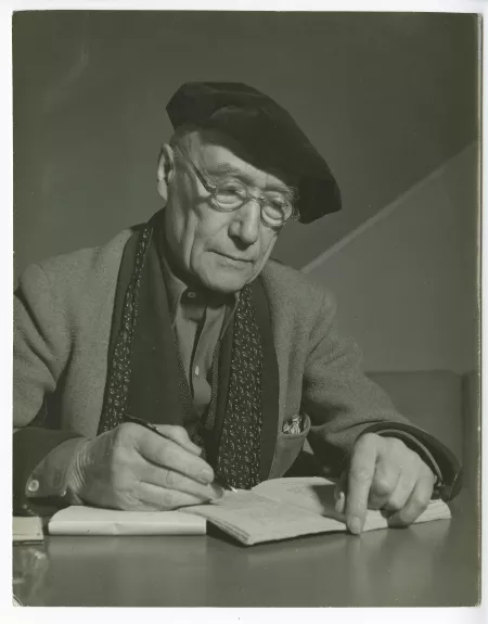 portrait photographique en buste d’André Gide, avec lunettes et béret, attablé, écrivant, chez Richard Heyd, hiver 1947