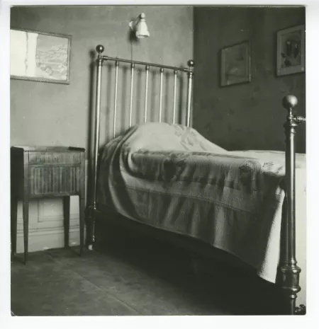 photographie du lit et de la table de chevet dans la chambre d'André Gide, avec les pastels de Simon Bussy accrochés au mur de droite, après sa mort, au Vaneau