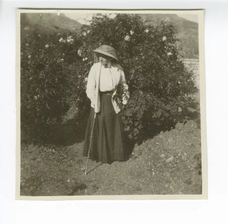 photographie de Maria Van Rysselberghe, debout devant un buisson de roses, dans le cimetière de Taormina, décembre 1908