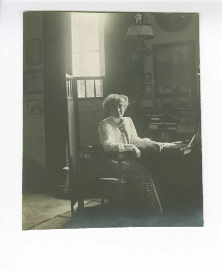 portrait photographique de Maria Van Rysselberghe, assise à un secrétaire, avec au mur un portrait dessiné d'Émile Verhaeren par Théo Van Rysselberghe (1892), à la villa Aublet, rue Laugier