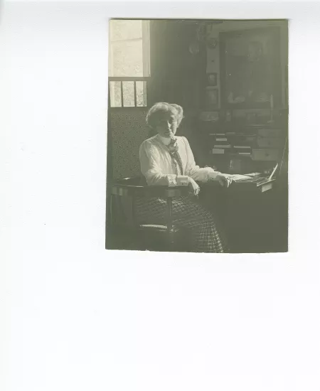 portrait photographique de Maria Van Rysselberghe, assise à un secrétaire, avec au mur un portrait dessiné d'Émile Verhaeren par Théo Van Rysselberghe (1892), à la villa Aublet, rue Laugier