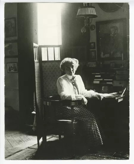 portrait photographique de Maria Van Rysselberghe, assise à un secrétaire, avec au mur un portrait dessiné d'Émile Verhaeren par Théo Van Rysselberghe (1892), à la villa Aublet, rue Laugier