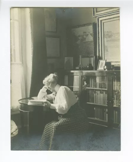 portrait photographique de Maria Van Rysselberghe, assise à côté d'une bibliothèque, lisant, dans la maison de la rue Laugier