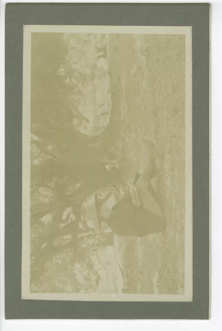 portrait photographique de Lucie Delarue-Mardrus, assise, lisant devant un grand arbre