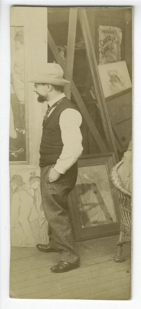 photographie d'Henri de Toulouse-Lautrec, dans son atelier, devant Au salon de la rue des Moulins (1894) accroché au mur, à ses pieds à gauche, Alfred la Guigne (1894), et à droite, sous verre, La Femme aux gants (1890)