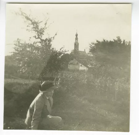 photographie de Daisy Weber, assise dans l’herbe, avec en arrière-plan l'hôtel de ville