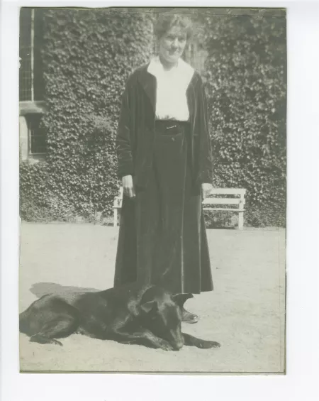 portrait photographique en pied de Suzanne Schlumberger, un chien couché à ses pieds, devant la propriété de ses parents, le château de Bois-Salair