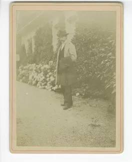 photographie d’André Gide, avec moustache et chapeau, en extérieur, portant un manteau à la main
