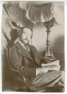 portrait photographique d’André Gide assis, à la barbe en double pointe, un livre entre les mains, pendant son voyage en Afrique du Nord, février-mars 1894