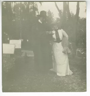 photographie d’André Gide, avec moustache et chapeau, lisant, et Maria Van Rysselberghe, en blanc, dans un cimetière, août 1903