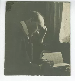 portrait photographique d’André Gide, assis à son bureau de la villa Montmorency, écrivant, sous le masque mortuaire de Leopardi, mai 1910