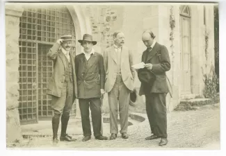 photographie de groupe avec, de gauche à droite, Jean Schlumberger, Jacques Copeau, Edmund Gosse, et André Gide, lisant, une raquette de tennis sous le bras, décade de Pontigny, août 1912