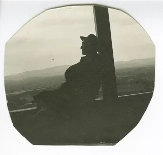 photographie d’André Gide, assis, le dos appuyé contre un pilier, bras croisés, sur le balcon d'une loggia à Brousse, en Anatolie, mai 1914