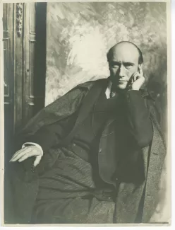 portrait photographique d’André Gide, assis, de face, devant une toile peinte