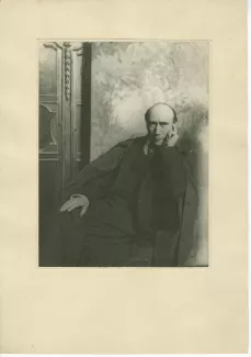 portrait photographique d’André Gide, assis, de face, devant une toile peinte