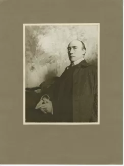 portrait photographique d’André Gide, assis, de ¾, mains jointes, devant une toile peinte
