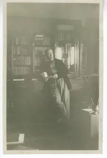 photographie d’André Gide, debout, livre à la main, devant une bibliothèque, chez les Mayrisch à Dudelange, Pâques 1919