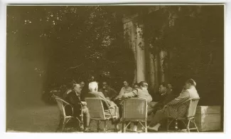 photographie montrant André Gide, assis à gauche de profil, Léopold Chauveau, assis de dos (cheveux blancs), André Malraux, assis de dos (tourné vers Gide), Roger Martin du Gard, assis à droite, de profil (veste à rayures), et des anonymes, août 1928
