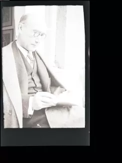 portrait photographique d'André Gide, avec lunettes, lisant, cigarette dans la main droite, juillet 1931