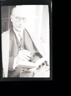 portrait photographique d'André Gide, presque de face, avec lunettes, lisant, cigarette dans la main droite, juillet 1931