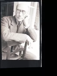 portrait photographique d'André Gide, avec lunettes, la main gauche sur la joue, à califourchon sur une chaise, juilet 1931