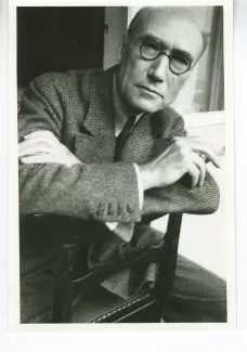 portrait photographique d'André Gide, presque de face, avec lunettes, cigarette dans la main gauche, à califourchon sur une chaise, juillet 1931